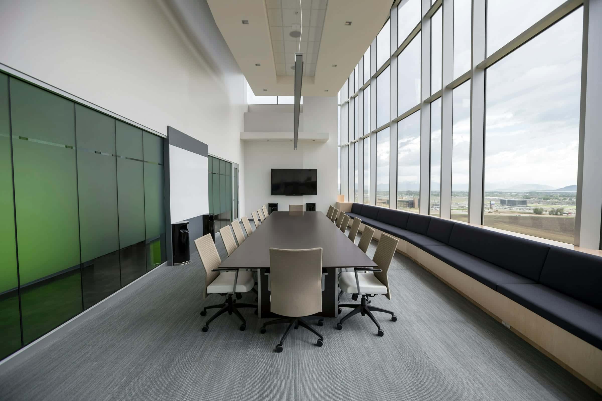 An empty boardroom with a long table beside floor-to-ceiling windows.