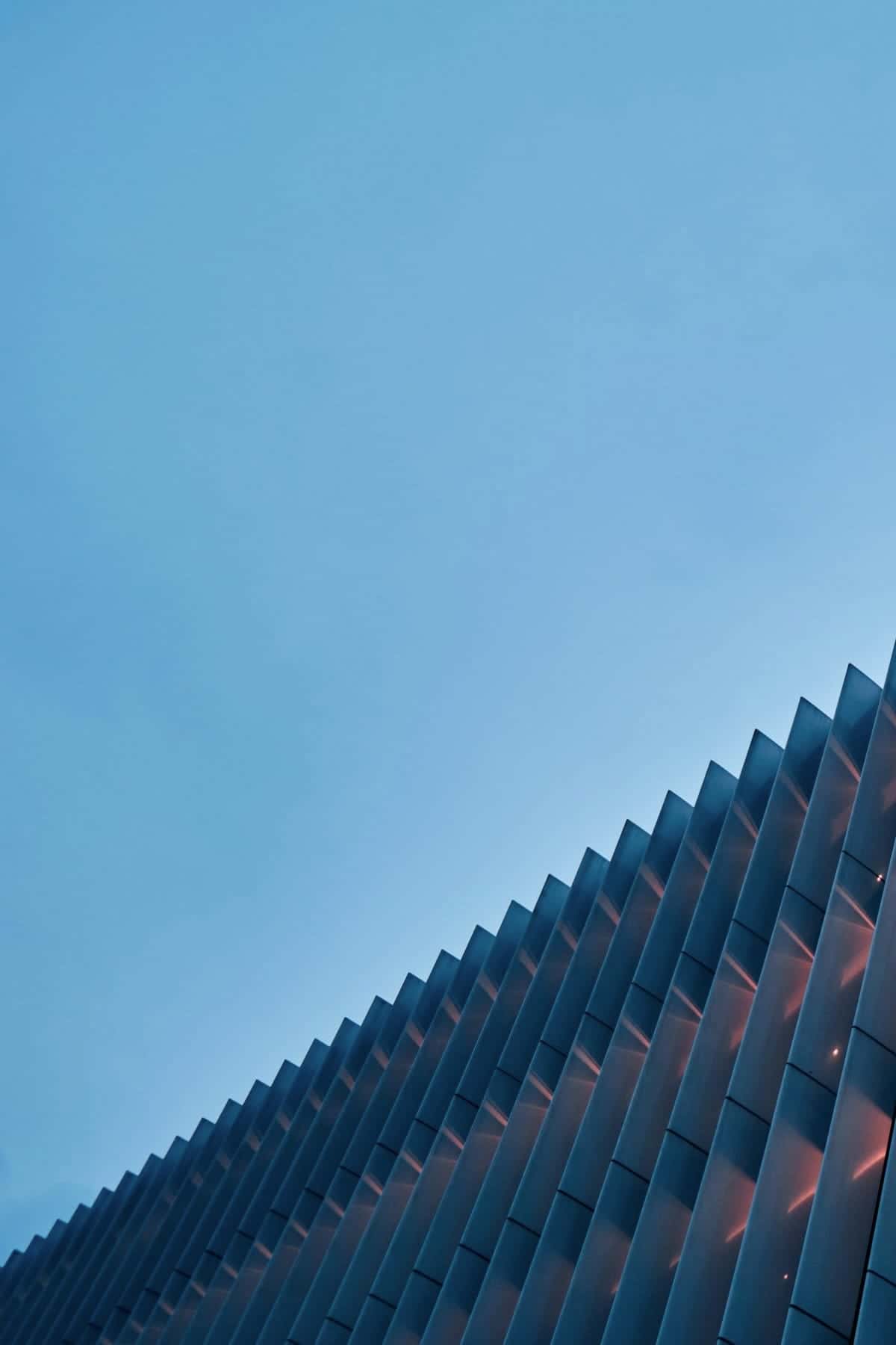 A building facade of tall vertical fins, lit from within, against a blue evening sky.