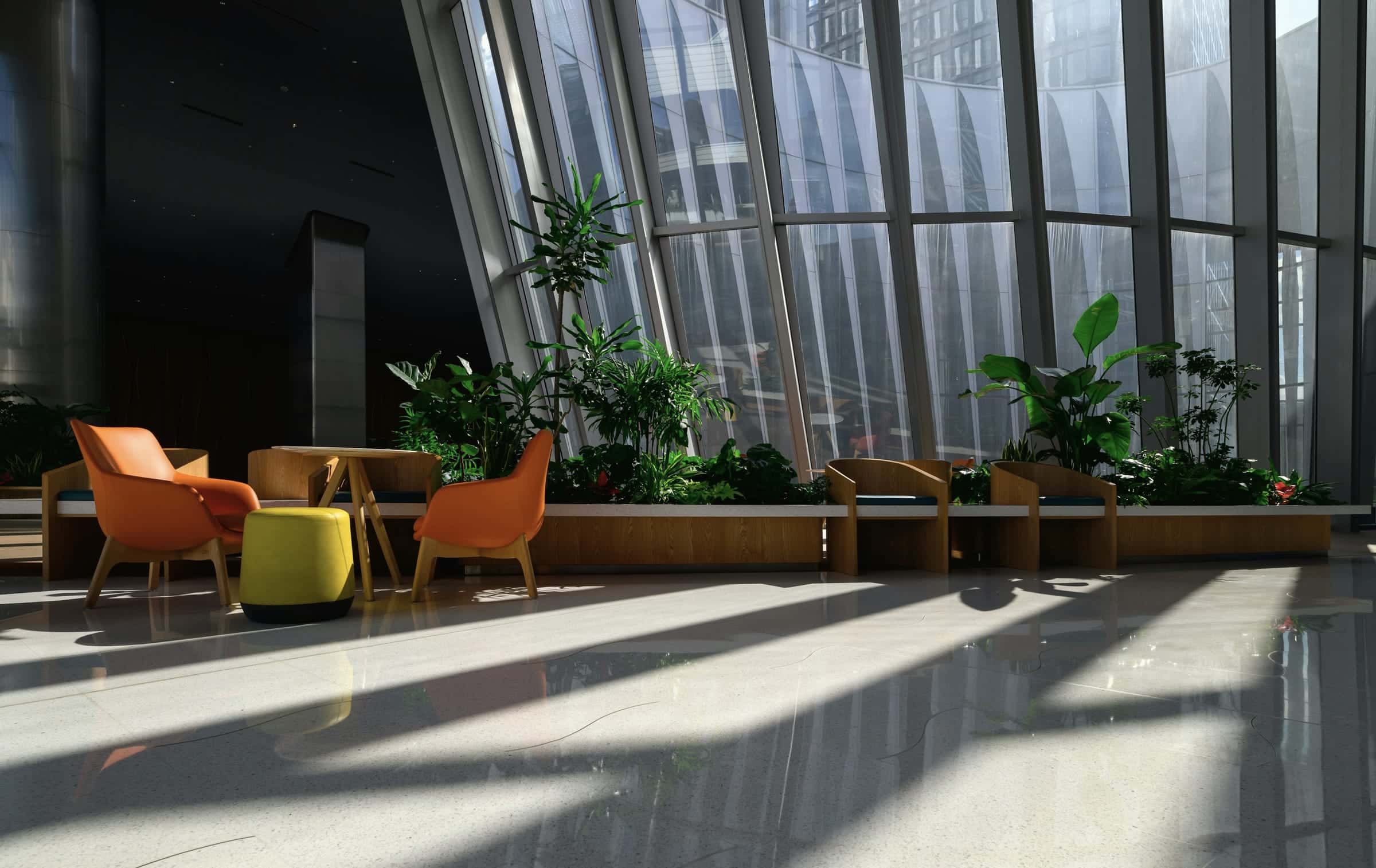 A sunlit lounge with orange chairs and planters beside a tall, sloping glass wall.