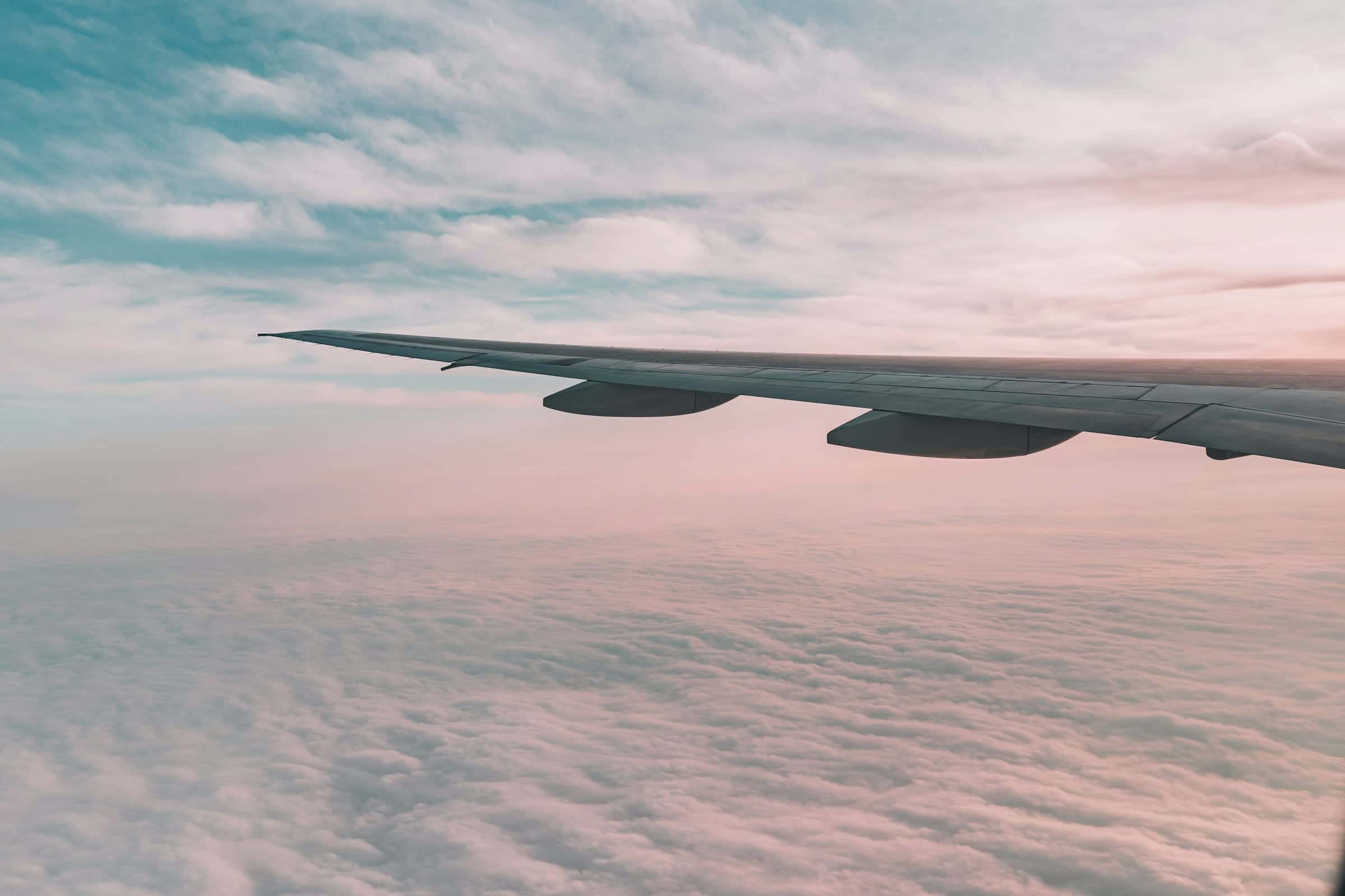 An aircraft wing above a layer of pink and white cloud.