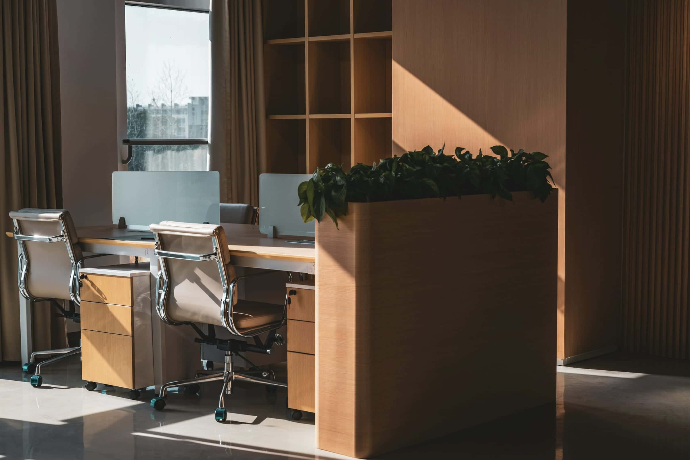 Desks and chairs beside a wooden planter in warm window light.