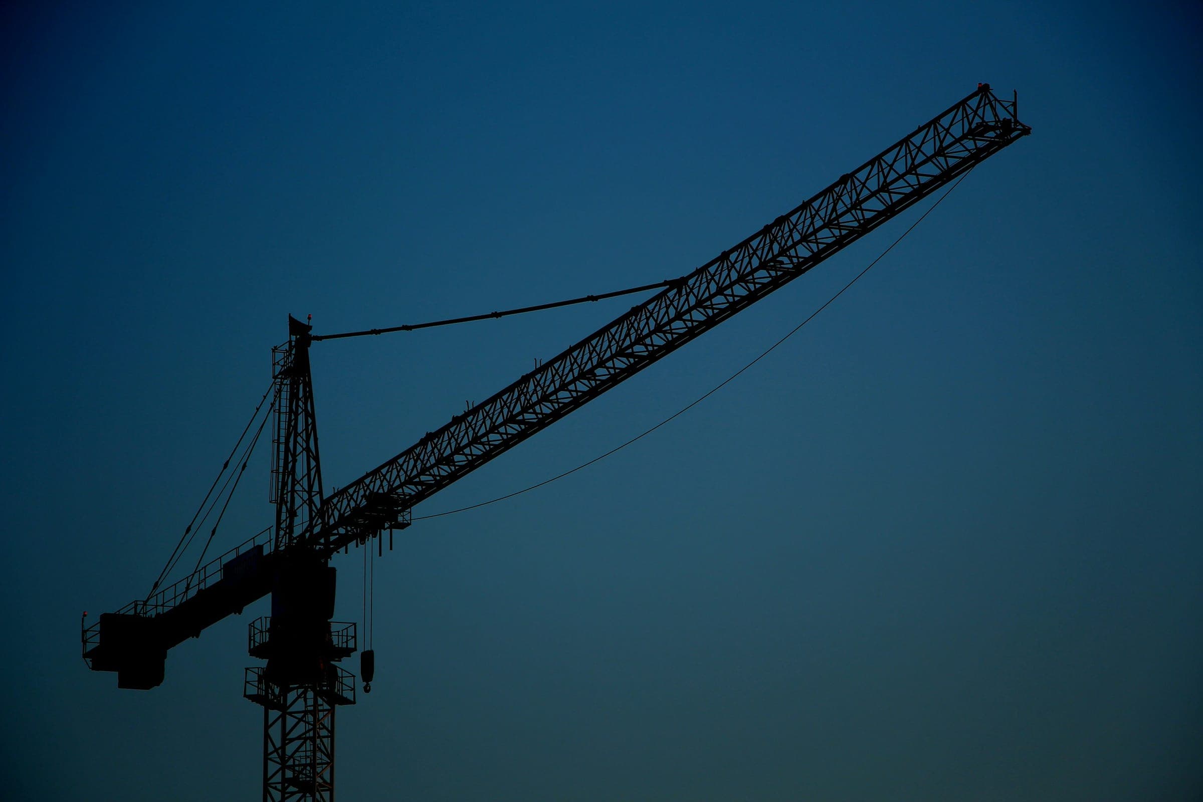 The silhouette of a tower crane against a deep blue evening sky.