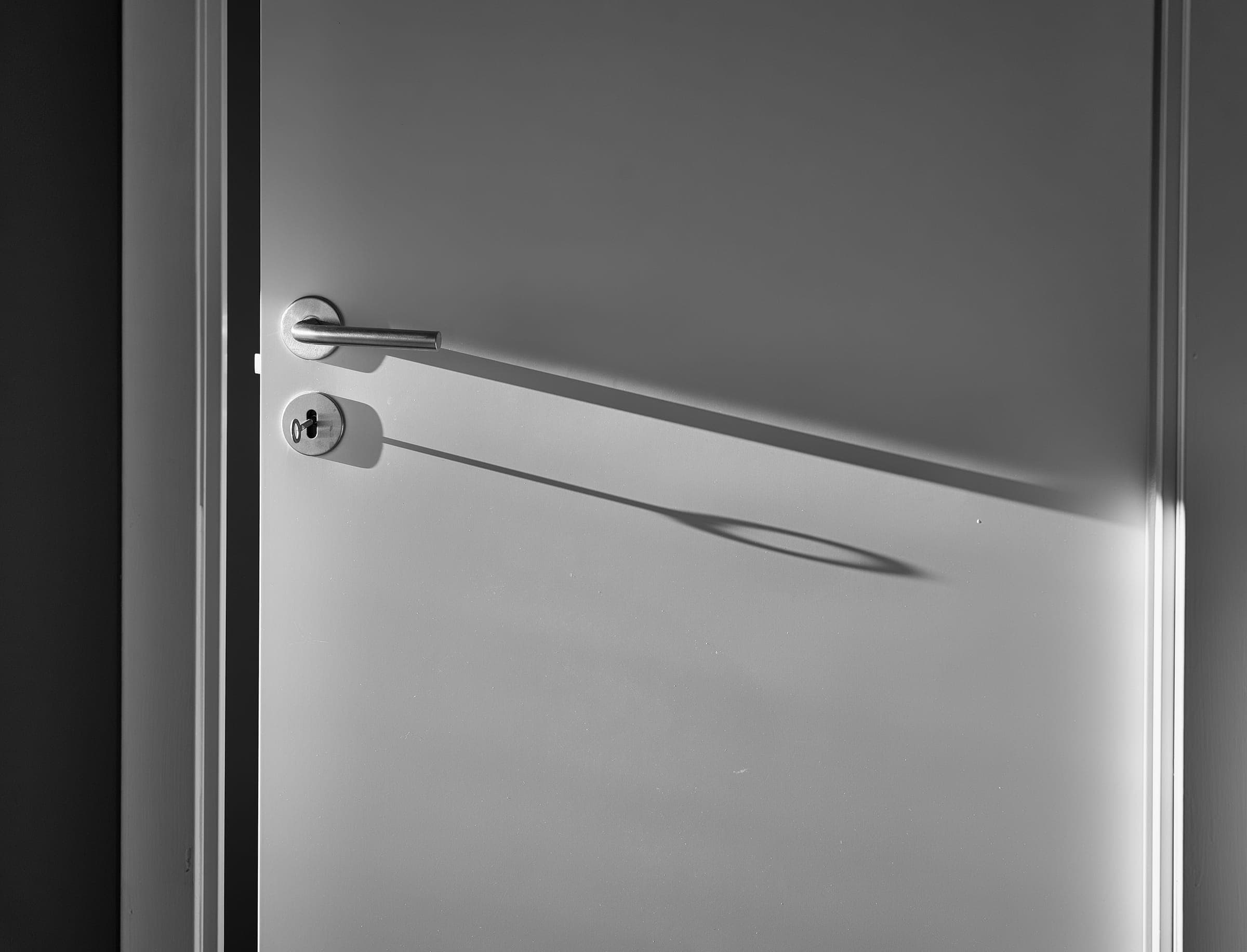 A brushed steel lever handle on a pale grey door, casting a long shadow in low light.