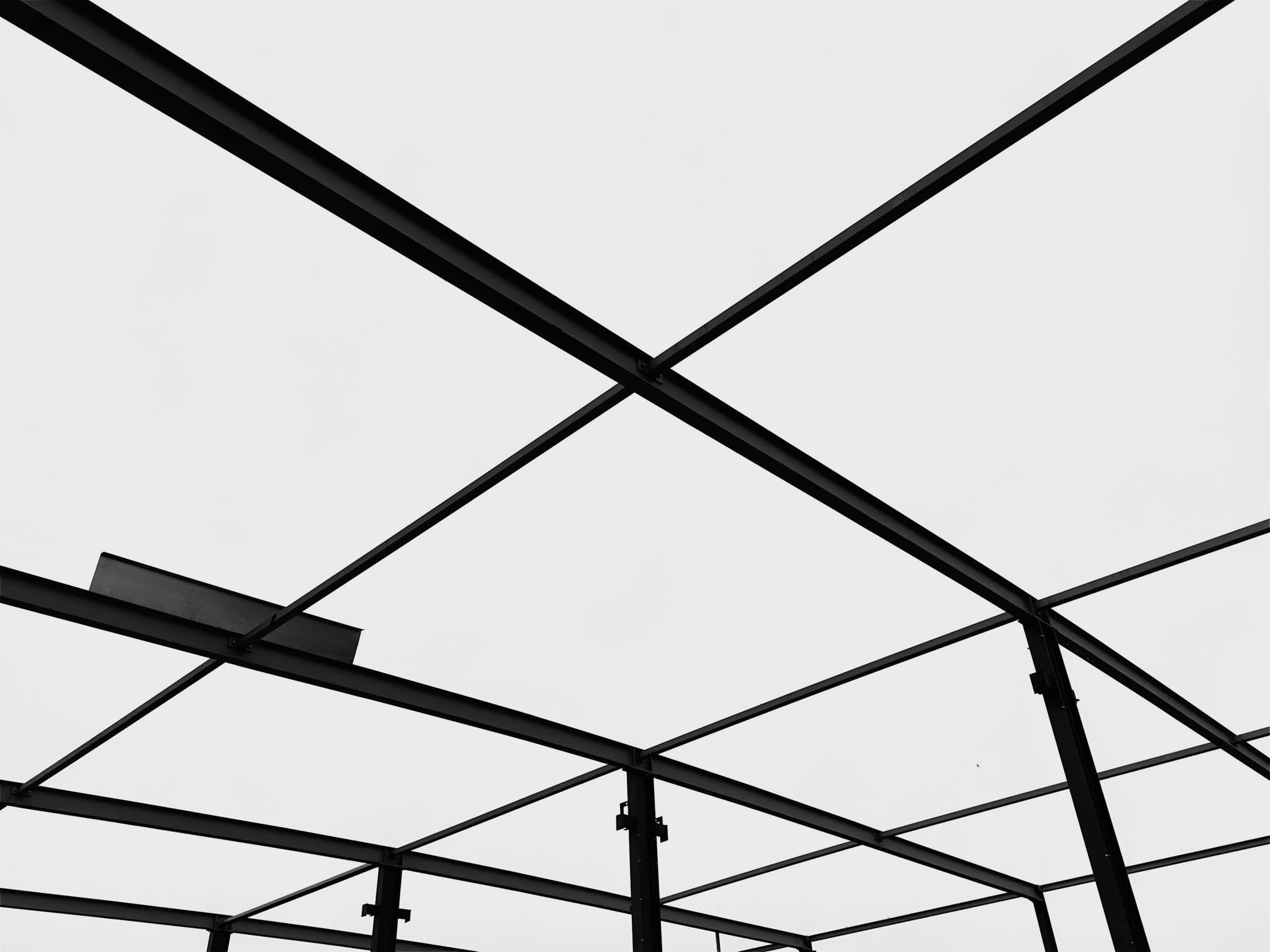 A black steel frame of beams and columns against a pale sky.